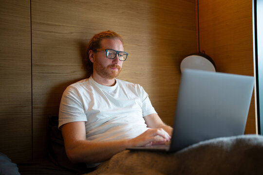 Man works on laptop while sitting on bed in a private room
