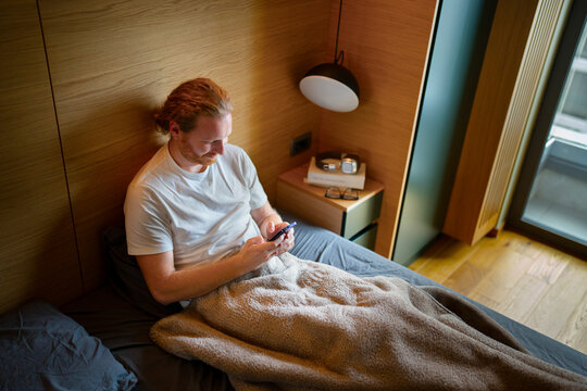Man using smartphone while sitting on bed in modern room
