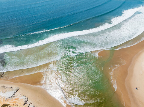 Waves in a turquoise ocean rolling into a coastal rivermouth