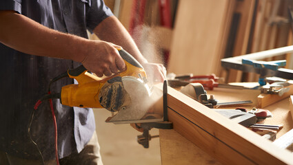 Woodworker's hands with yellow circular saw