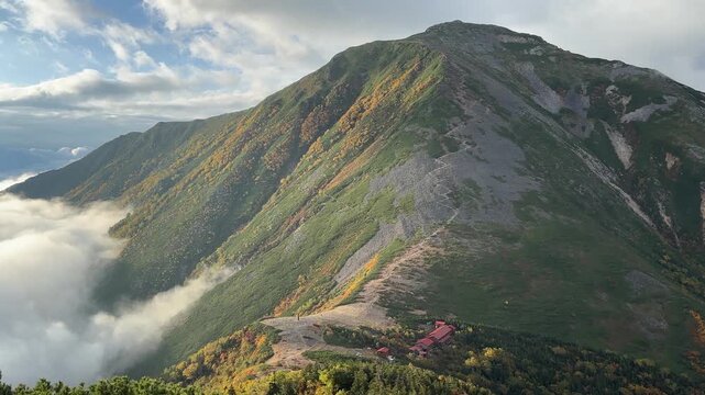 Jonengoya hut in the Northern Japanese Alps, surrounded by rugged ridges and autumn foliage, bathed in soft morning light with a sweeping mountain panorama.