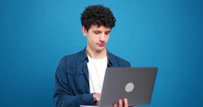 Smiling man using laptop, copywriter typing on keyboard, freelancer working on blue background