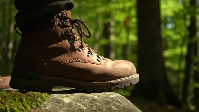 A captivating close-up shot focuses on a sturdy brown leather hiking boot resting firmly on a moss-covered rock, bathed in dappled sunlight filtering through a vibrant green forest canopy. The boot's 