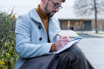 Young man writing notes in notebook in city