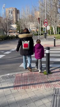 Madre e hija cruzando paso de peatones de la mano por la calle juntas