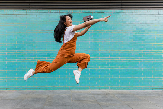 Excited director holding vintage camera jumping and pointing outdoors