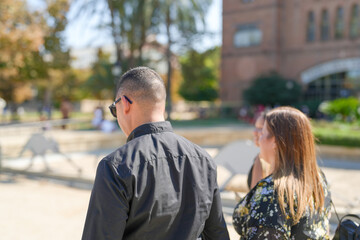 Fototapeta premium A man in a black shirt and sunglasses is walking past a woman in a floral dress. Scene is casual and relaxed, as the two people are enjoying a leisurely stroll together