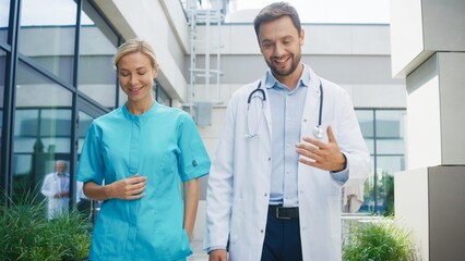 Smiling female nurse walking beside focused male doctor outside clinic. Confident pair discussing duties while moving along pathway. Professional team sharing thoughts during relaxed moment.