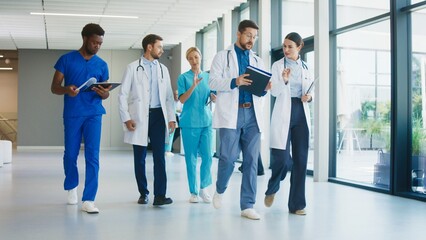 Medical staff walking calmly along bright corridor inside modern hospital. Focused doctors reviewing notes while discussing plans. Nurses joining conversation and moving together during routine moment
