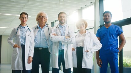 Medical team posing proudly in bright hospital corridor. Standing with confident expressions. Showing teamwork spirit and presenting strong professional image during active clinical routine.