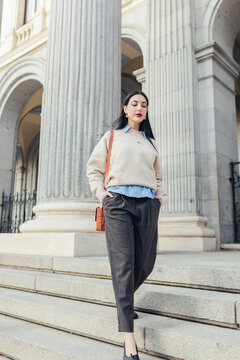 Woman walking down steps with hands in pockets outside Madrid colonnade