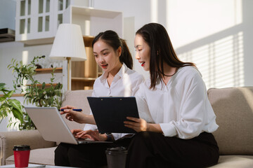 Two Asian women are reviewing and discussing a business project that involves working online from home office.