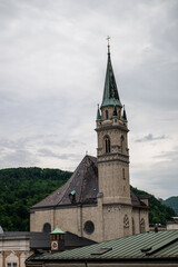Obraz premium Historic church tower rising above Salzburg old town rooftops with green alpine hills in background