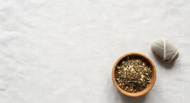 Dried Greek herbal tea mix in a wooden bowl next to a striped pe