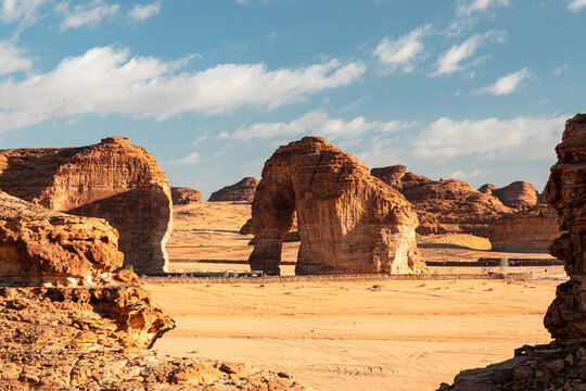 Desert Elephant Rock (Jabal Al Fil) arches rise from golden sand under clear blue sky, timeless landscape