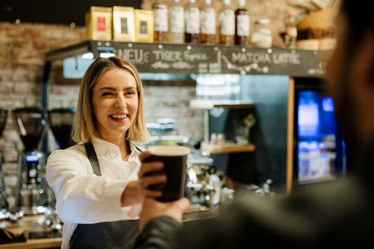Smiling barista handing coffee to customer inside modern cafe