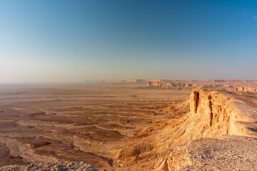 Sunlit desert canyon cliffs Edge of the World in Saudi Arabia at dusk, vast arid landscape with terraced rock formations