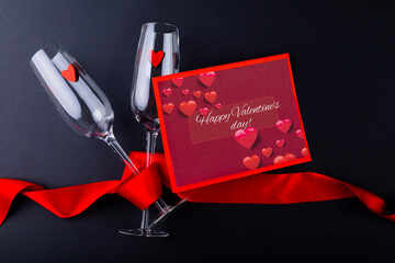 Valentines day gift card by champagne flutes wrapped with red ribbon on black table with copy space