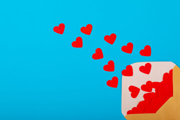 Open beige envelope with red heart shapes by copy space over blue background