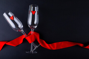 Heart shapes in empty champagne flutes wrapped with red ribbon by copy space over black background