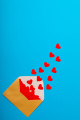 Overhead view of open beige envelope with red heart shapes by copy space over blue background