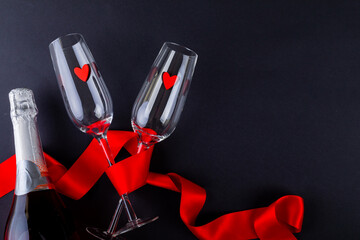Heart shapes in empty flutes wrapped with red ribbon by champagne bottle