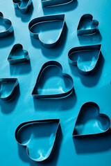 High angle view of heart shape pastry cutters with shadows on blue background