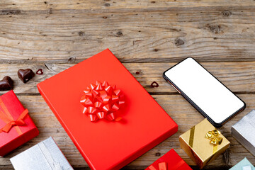 Blank screen on mobile phone with copy space arranged by gift boxes on wooden table