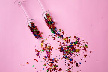 Overhead view of champagne flutes with scattered multi colored confetti on pink background