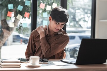 Young man experiencing shoulder pain while working at laptop desk