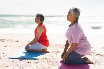 Senior couple practicing kneeling yoga pose while meditating on exercise mat at beach