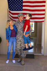 Happy caucasian family with army soldier standing at the entrance of house with usa flag