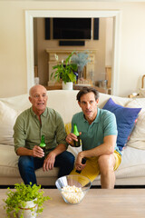Caucasian father and son with beer watching tv together on the couch at home
