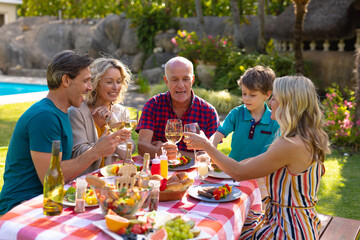 Fototapeta premium Happy caucasian family toasting drinks while sitting together at table in garden