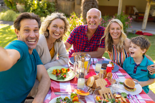 Portrait of cheerful caucasian family taking selfie at table in the garden