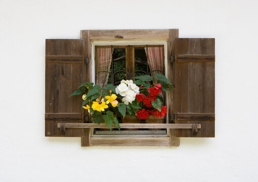 Farmhouse window with wooden shutters and colorful flowers in Styria Austria