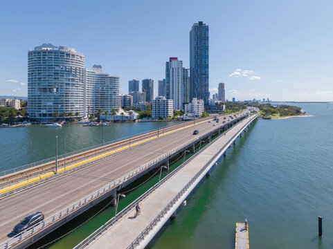 Aerial view of wide parallel bridges over coastal waterway leading to high-rise buildings
