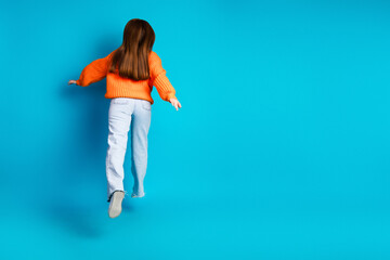 Young girl in orange knit sweater jumps against blue background for playful fashion and energetic...