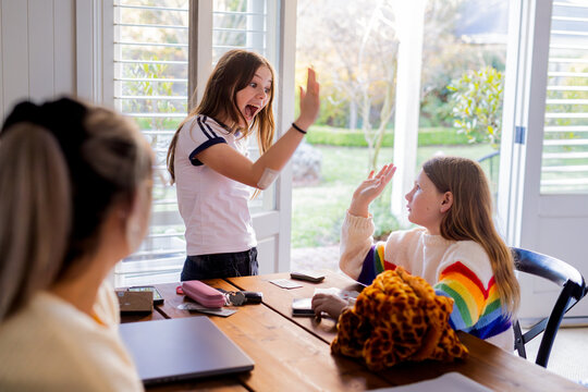 Young girls doing high five over the table while playing cards