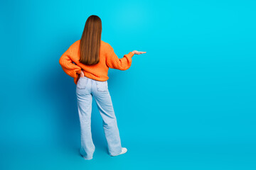 Young woman in orange sweater stands against blue background looking stylish and confident for...