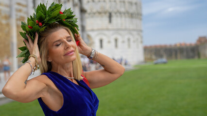 Elegant graduate walking under the Leaning Tower of Pisa wearing a laurel wreath in Piazzale dei...