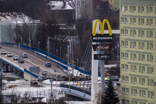 Polska, Ostrowiec Świętokrzyski, 31 grudnia 2025, 14:53. Logo McDonald's z mostem i wiaduktem w tle. Znak przedstawia charakterystyczne ż&oacute;łte łuki, a pod nim znajdują się znaki McCaf&eacute; i McDrive. 