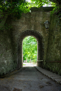 Scenic stone arch tunnel pathway surrounded by lush green trees in historic European park 