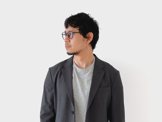 Man wearing a gray suit and glasses stands in front of a white wall