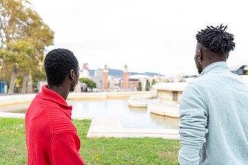 Two black men enjoying Barcelona city views from a park fountain area