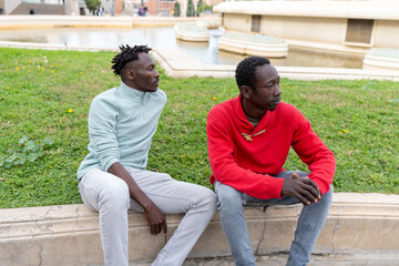 Two young African men sitting on the grass edge in a Barcelona city park, lifestyle