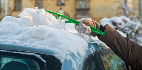 Person sweeping fresh white snow off a blue automobile windshield and top after a blizzard. Seasonal morning routine and cold weather care. Photo