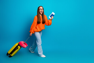 Young woman in orange sweater travels with bright suitcase and passes passport against blue...