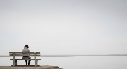 Person sitting alone on bench looking at vast calm horizon over the ocean during overcast day