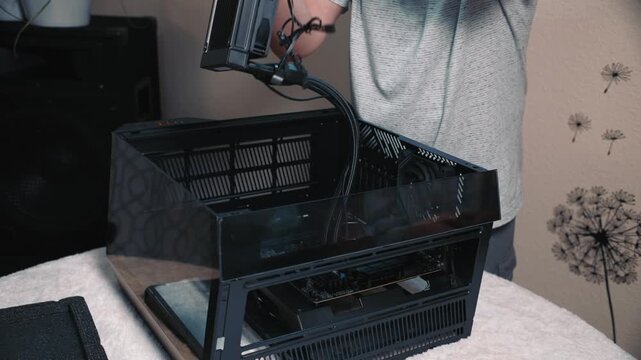 Installing liquid cooling system into compact computer case, personal PC build process showing close-up of male hands carefully placing radiator with fans inside a transparent chassis
